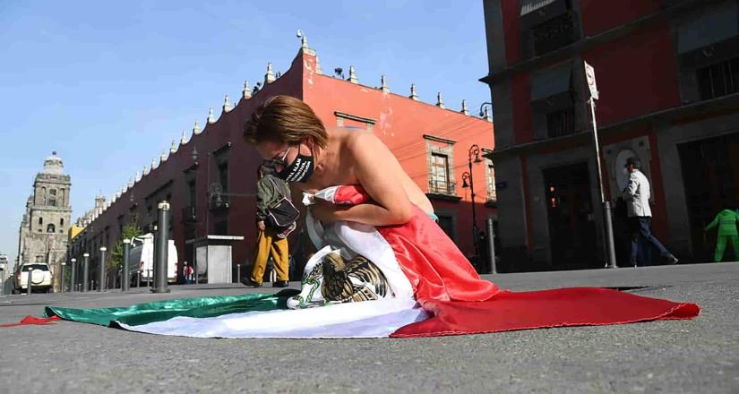 Mujer envuelta en bandera frente a Palacio Nacional exige justicia.